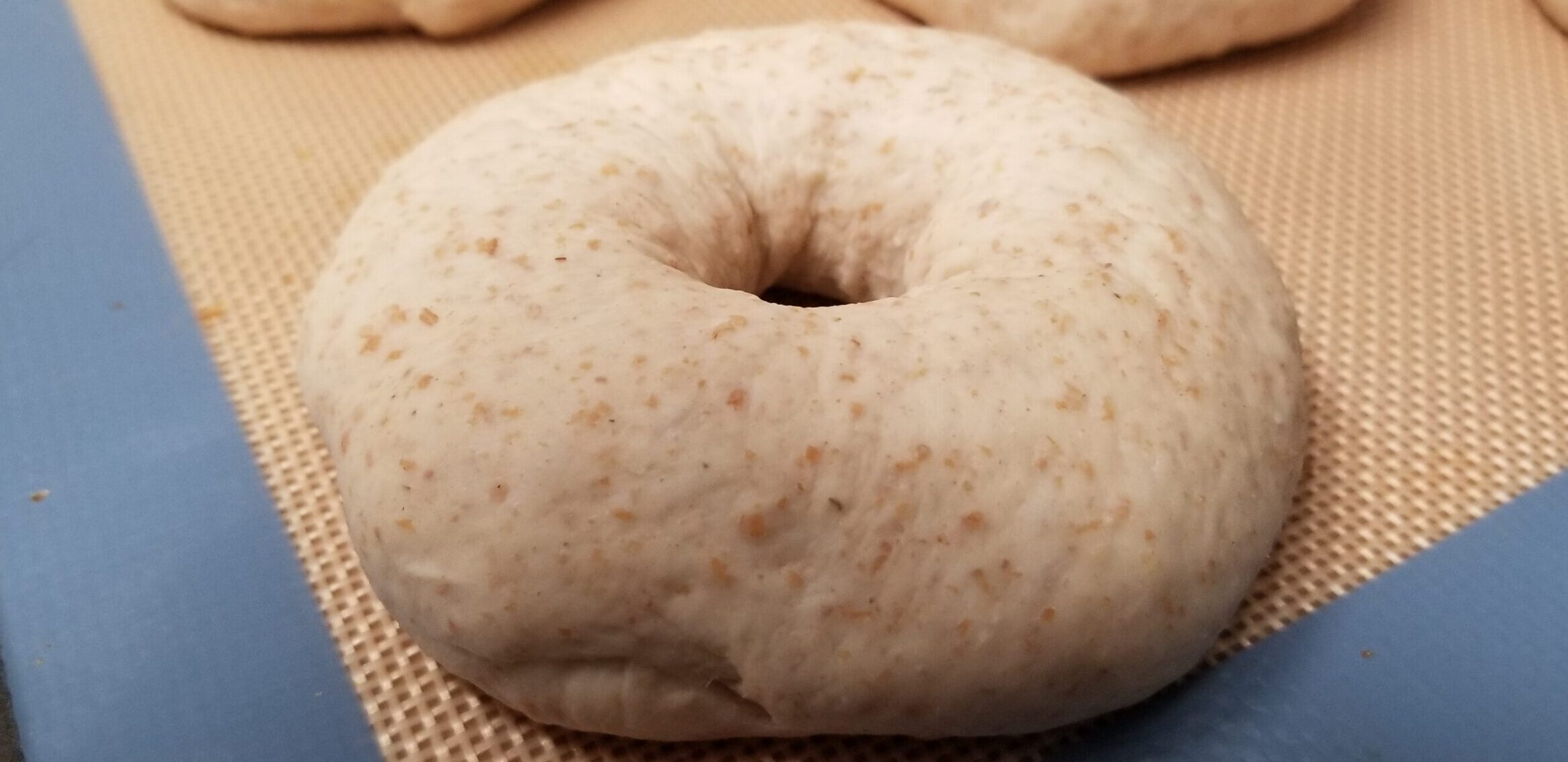 An unbaked bagel sitting on a silicone baking mat, ready to be boiled.