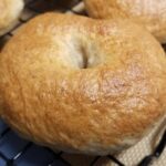 A freshly baked, golden brown bagel cooling on a wire rack with its friends.
